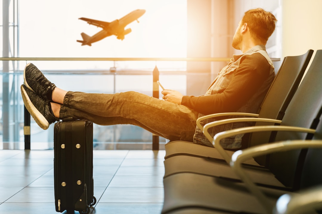 man-sitting-on-gang-chair-with-feet-on-luggage-looking-at-airplane-mseswdmzr-a